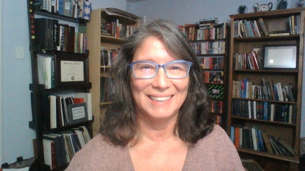 a square photo of Carola E. Morton, a smiling woman with wavy, shoulder-length hair and glasses