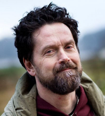 Photo of Stellan Vinthagen, a man with short, dark hair and a brown beard in a red shirt and brown coat.