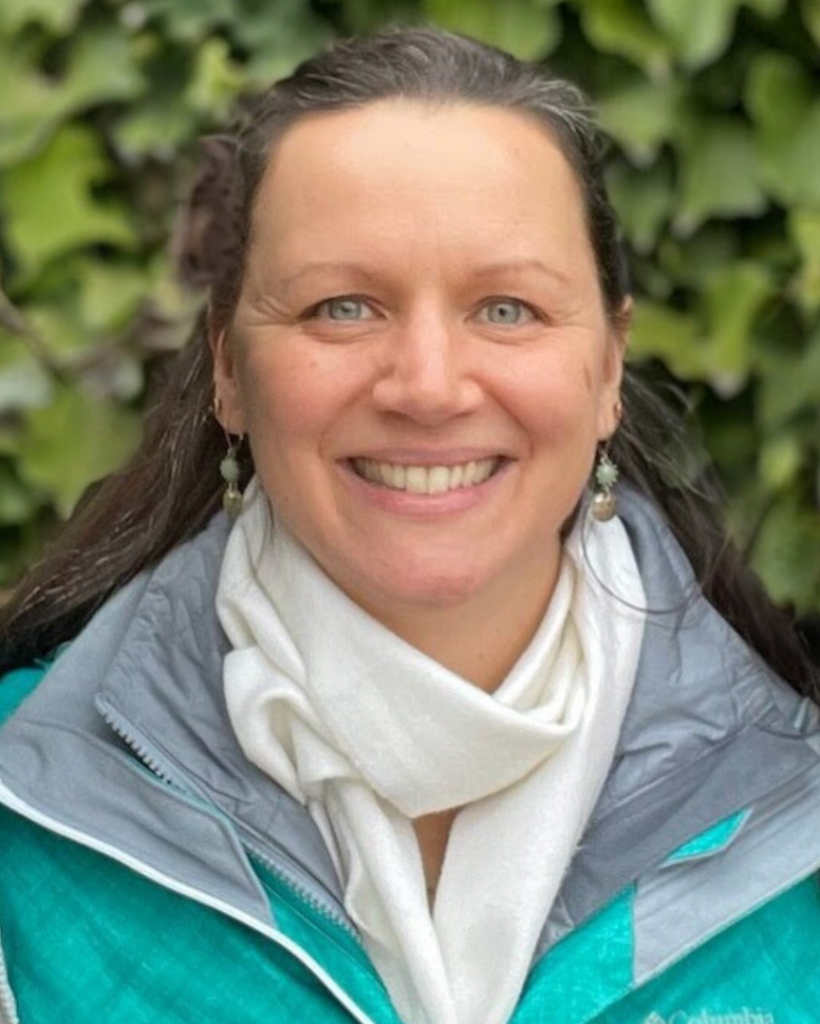 Photo of Amanda Wheeler-Kay, a smiling, blue-eyed woman with long brown hair wearing a white scarf and light green coat.