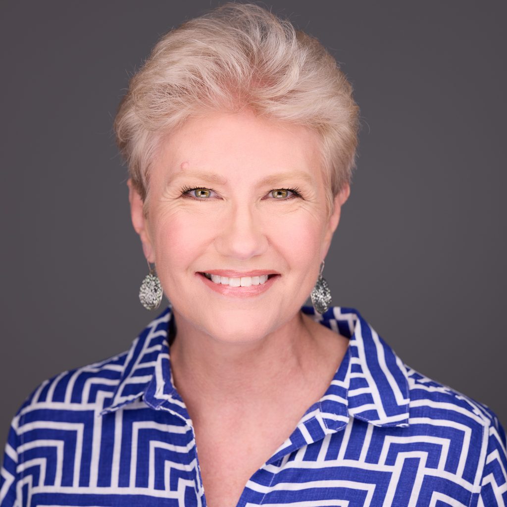 Photo of Dr. Holly Silvestri, a blue-eyed woman with short blonde hair, wearing a blue and white patterned top and earrings.