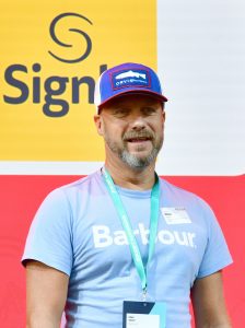 Photo of Mark Applin, a man with a gray beard in a blue hat with a white fish on it and a light blue shirt.