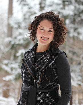 Photo of Su Kyong Isakson, a smiling woman with dark, curly hair in a black and white plaid outfit with gray sleeves